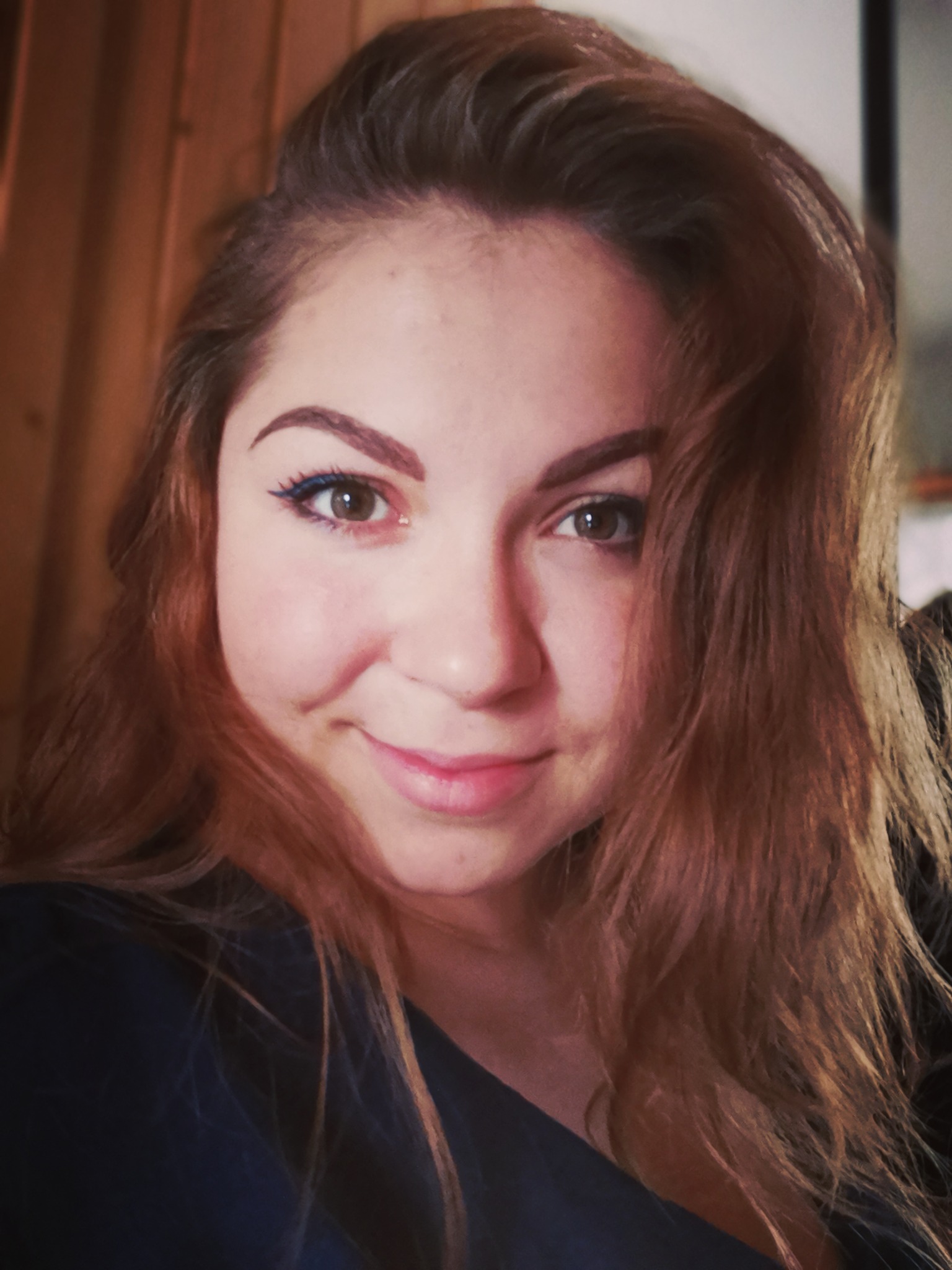 Portret uśmiechniętej kobiety z długimi, rudymi włosami i niebieskim eyelinerem.