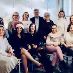 Grupowe zdjęcie zespołu doradców podatkowych w świątecznej atmosferze, jedna osoba w czapce Mikołaja, uśmiechnięci, w biurze z oknami w tle.