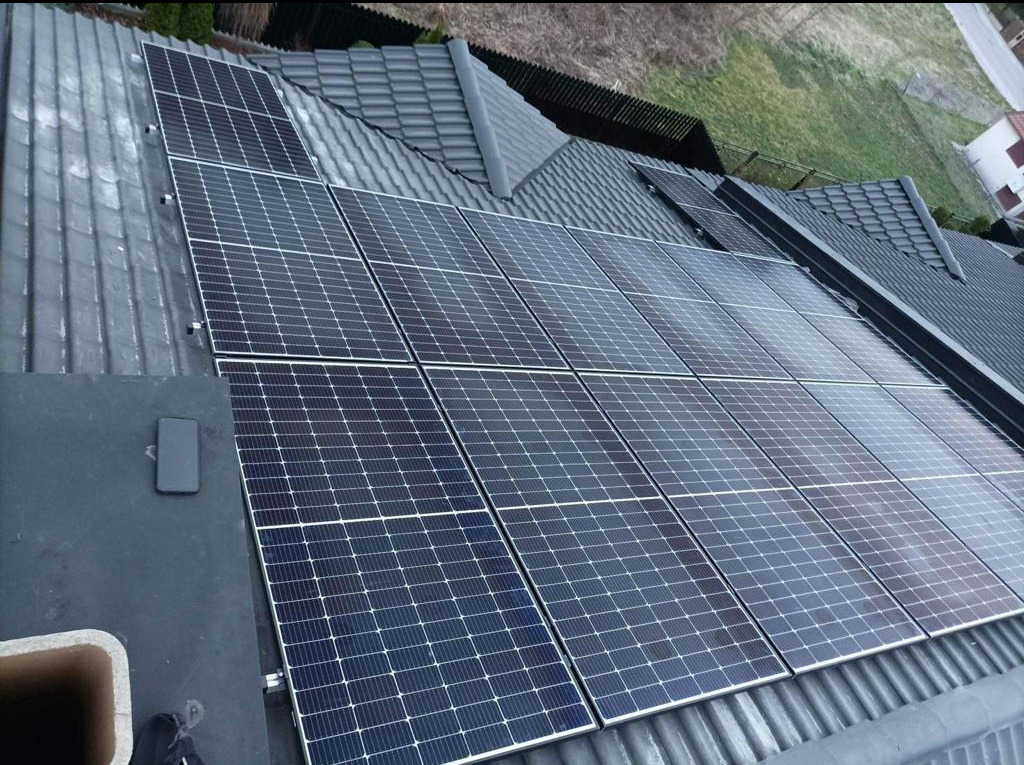 Panele fotowoltaiczne na dachu z szarej dachówki, widok z góry, telefon leżący obok paneli.