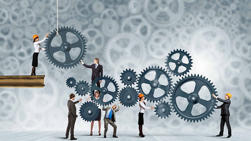 Zespół w kaskach i garniturach montuje system zębatych kół na tle abstrakcyjnego wzoru zębatek.