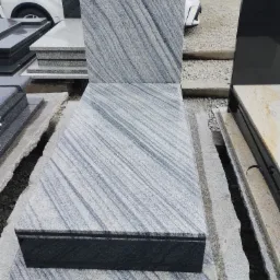 Wystawa elementów z jasnego, wzorzystego kamienia, prawdopodobnie przeznaczonych na pomniki, w Strzegomiu. Widoczne płyty i bloki kamienne o różnych wymiarach i wykończeniach.