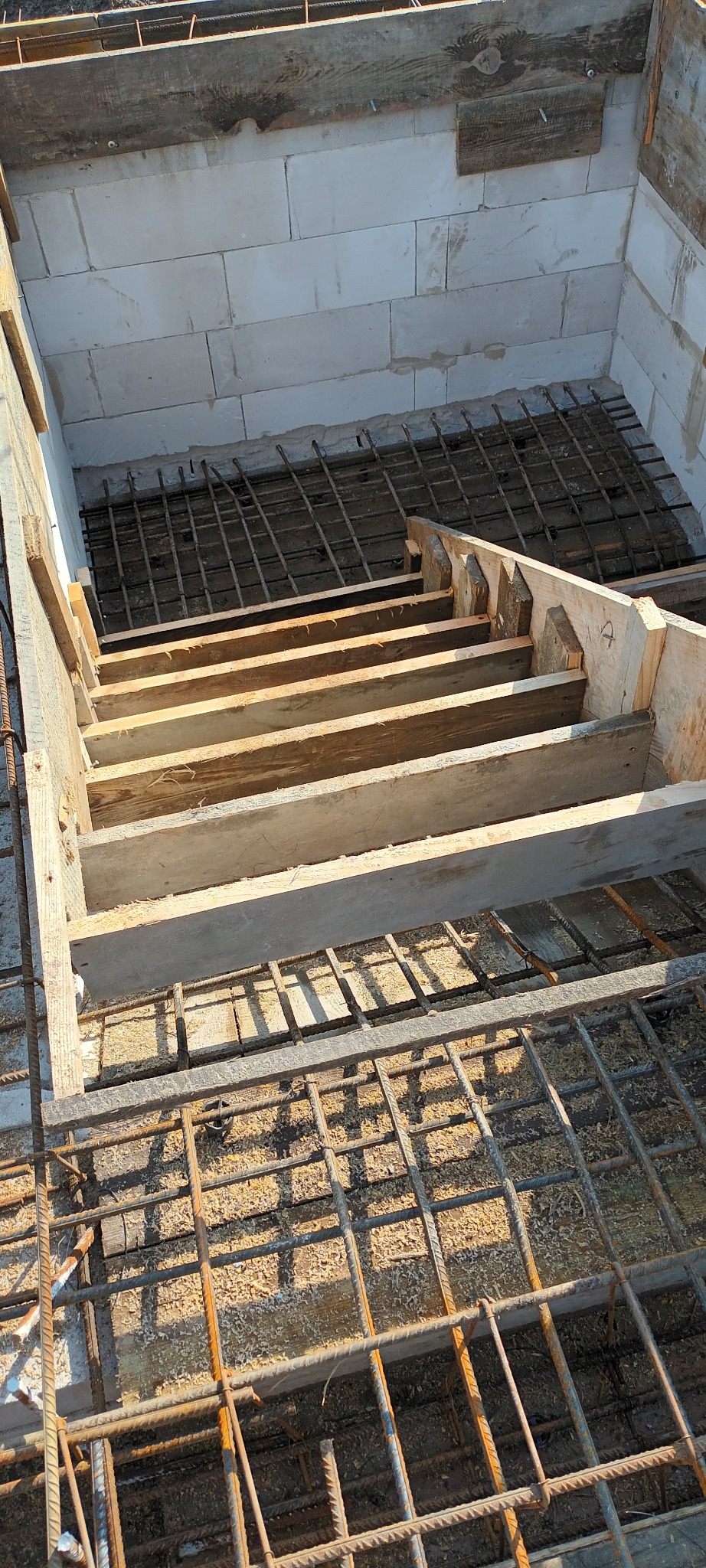 Wykop fundamentu z szalunkiem schodkowym, zbrojony stalową siatką i częściowo obłożony bloczkami betonowymi.