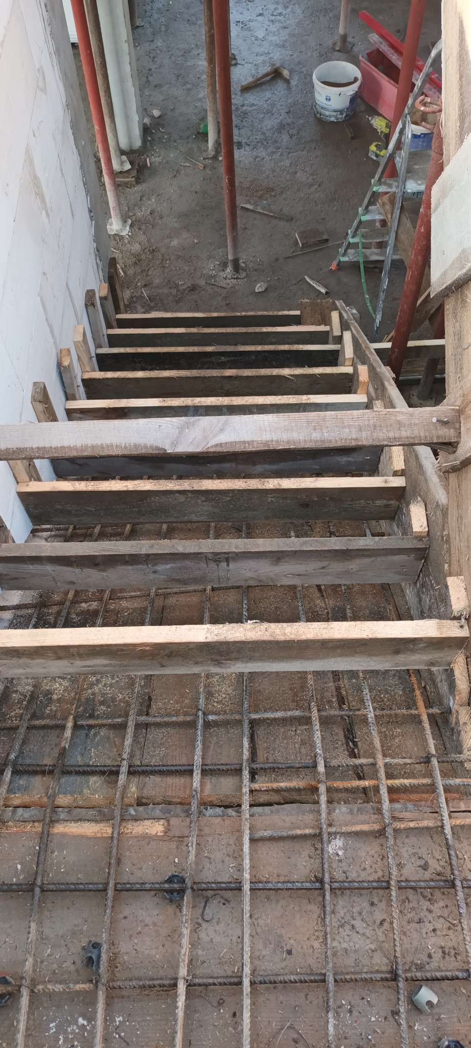 Konstrukcja drewniana szalunku schodów z widocznym zbrojeniem, przygotowana do zalania betonem, widok z góry na placu budowy.