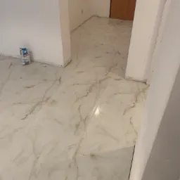 Jasne, marmurkowe panele podłogowe w korytarzu, z workiem zaprawy na tle ściany.