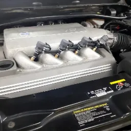 Silnik samochodu z zamontowanymi wtryskiwaczami, widoczne rury dolotowe i osprzęt, czarna pokrywa z naklejkami informacyjnymi.