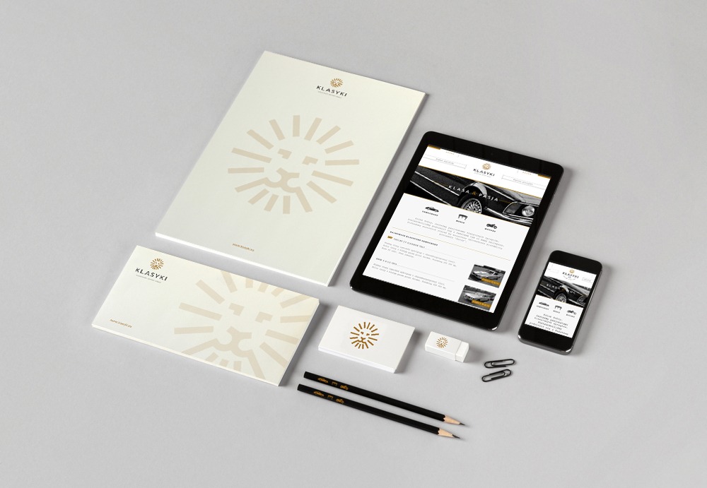 Identyfikacja wizualna firmy Klasyki: tablet i smartfon wyświetlające stronę internetową, papier firmowy, wizytówka, gumka, dwa ołówki i spinacze biurowe na jasnoszarym tle.