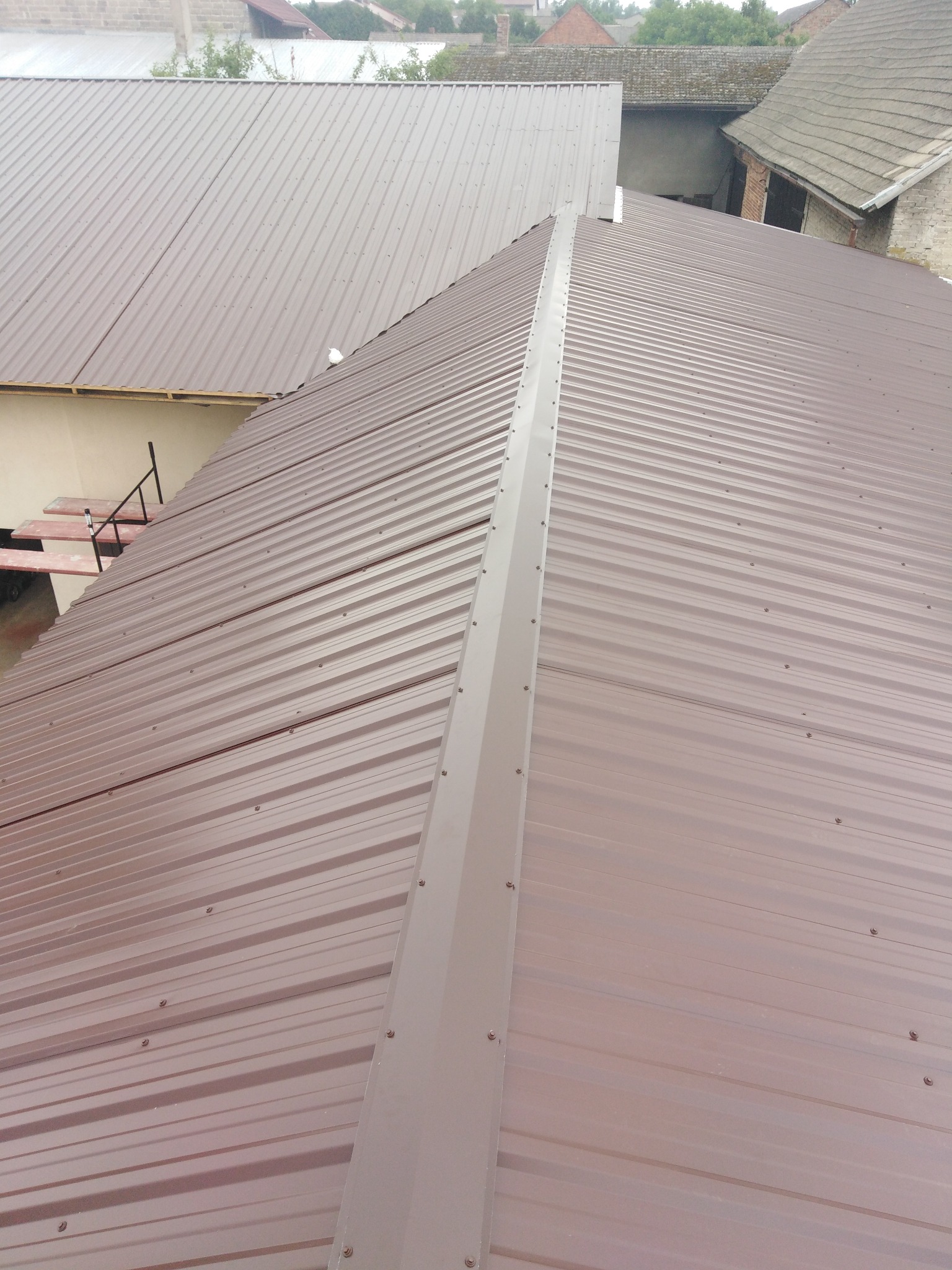 Nowy, brązowy dach z blachy trapezowej, widok z góry na kalenicę i sąsiednie budynki.