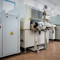 Profesjonalna linia produkcyjna JUKI KE-1080L i Solano RO 510 w jasnym pomieszczeniu, widoczne znaki ostrzegawcze.