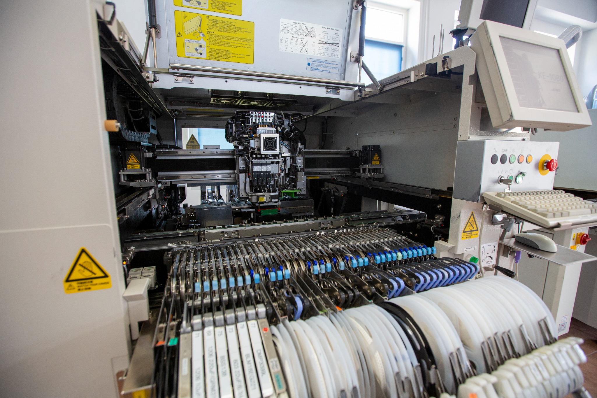 Widok z bliska na zaawansowaną maszynę do automatycznego montażu elementów elektronicznych z widocznymi podajnikami komponentów, głowicą montażową i panelem sterowania z klawiaturą i myszką.