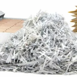 Pudełko archiwizacyjne z zawartością, sterta pociętych dokumentów i plik żółtych teczek na białym tle, ilustrujące proces przetwarzania dokumentów.