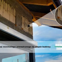 Montaż kamery monitoringu zewnętrznego na surowej ścianie budynku w trakcie budowy, widoczne drewniane elementy konstrukcyjne dachu i fragment okna, zbliżenie na kamerę w okręgu.