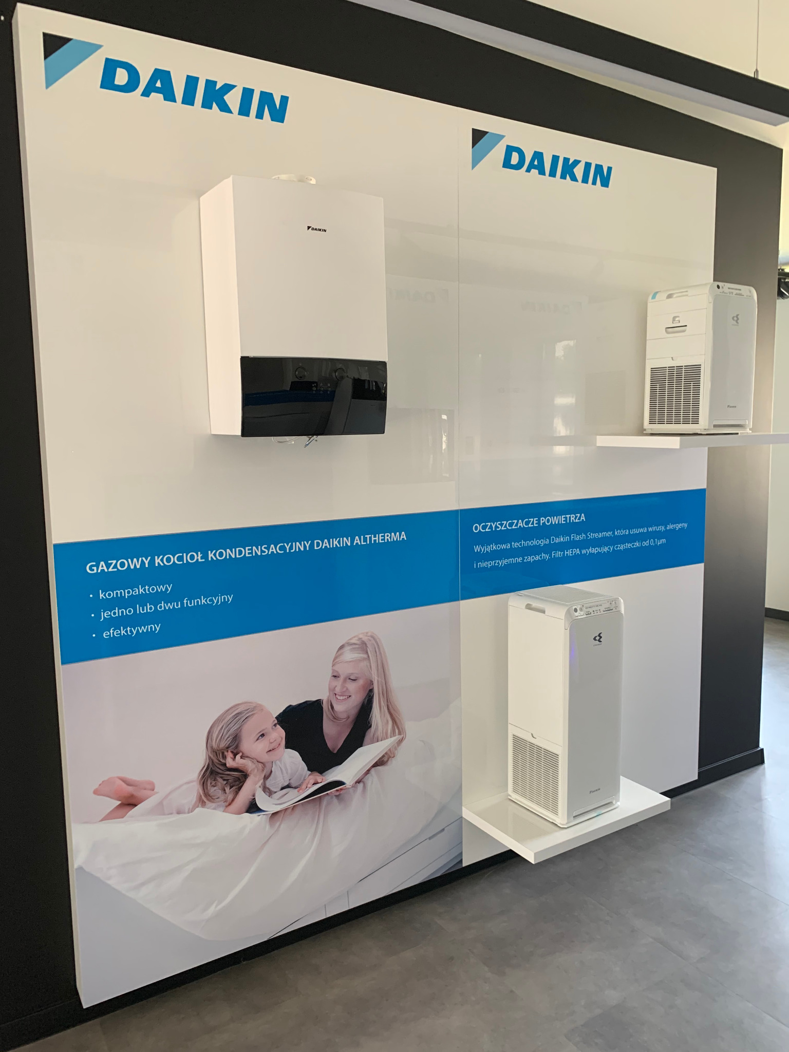 Ekspozycja produktów Daikin: gazowy kocioł kondensacyjny Altherma i oczyszczacze powietrza, prezentowane na białym panelu z informacjami o technologii Flash Streamer i filtrze HEPA. Na panelu...