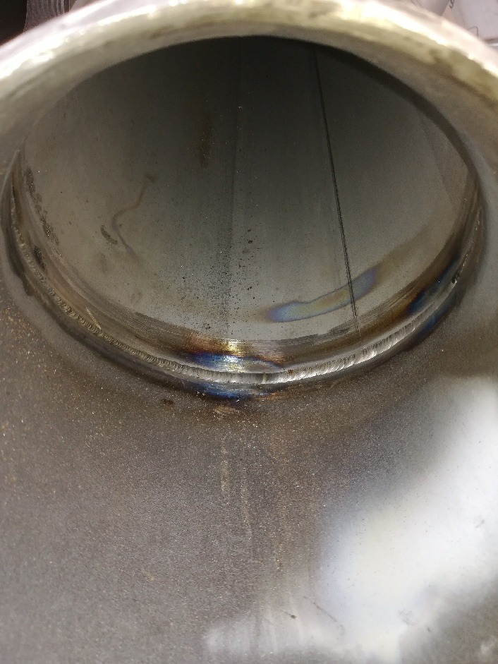 Wnętrze rury ze stali nierdzewnej z widocznym spoiną, na której widoczne są przebarwienia termiczne.