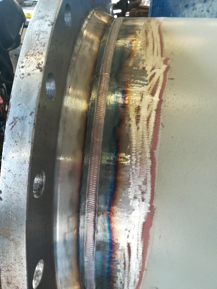 Spoina na metalowej rurze z kołnierzem, widoczne ślady obróbki termicznej i przebarwienia.