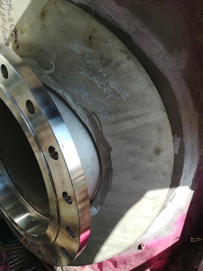 Spawana stalowa rura z kołnierzem, widoczne ślady spawania i oznaczenia techniczne.