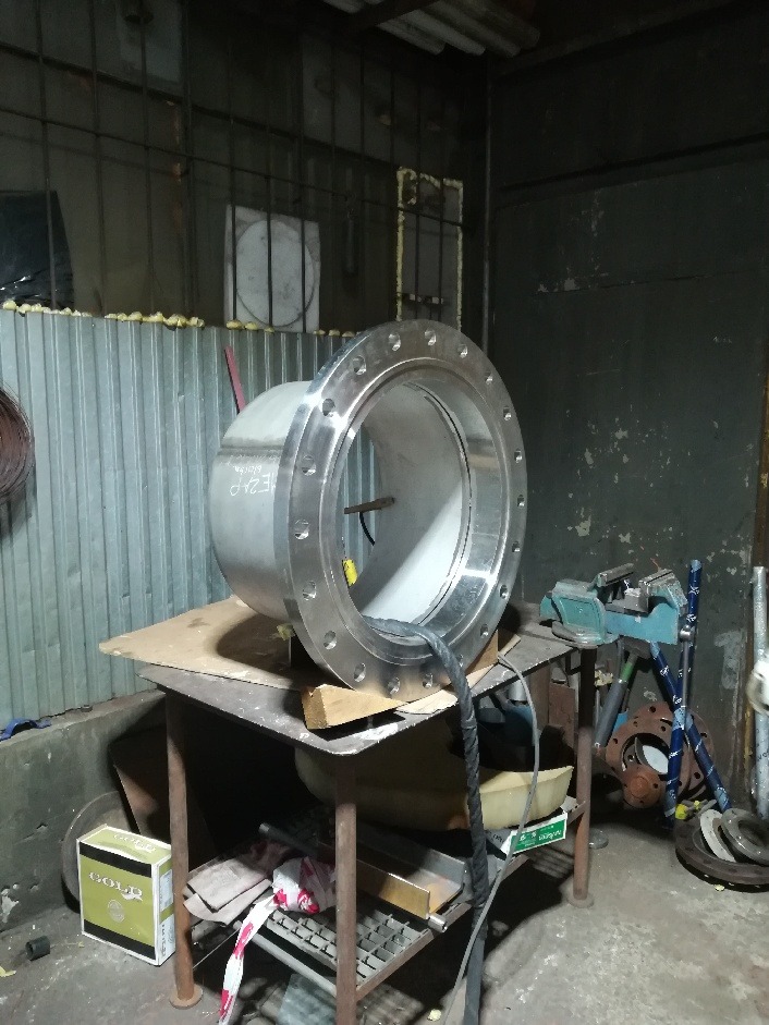 Szlifowany, metalowy element rurowy z kołnierzem, umieszczony na warsztatowym stole, widoczne ślady obróbki i niedoskonałości powierzchni.