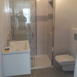 Dam-bud Damian Urbański - Nowoczesna łazienka z kabiną prysznicową typu walk-in, wiszącą szafką z umywalką, toaletą podwieszaną i dekoracyjnym pasem z motywem kamieni na podłodze.