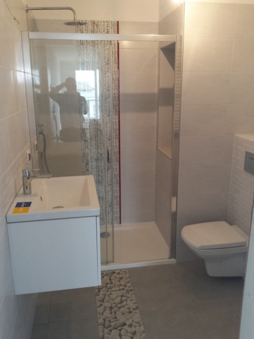 Nowoczesna łazienka z kabiną prysznicową typu walk-in, wiszącą szafką z umywalką, toaletą podwieszaną i dekoracyjnym pasem z motywem kamieni na podłodze.