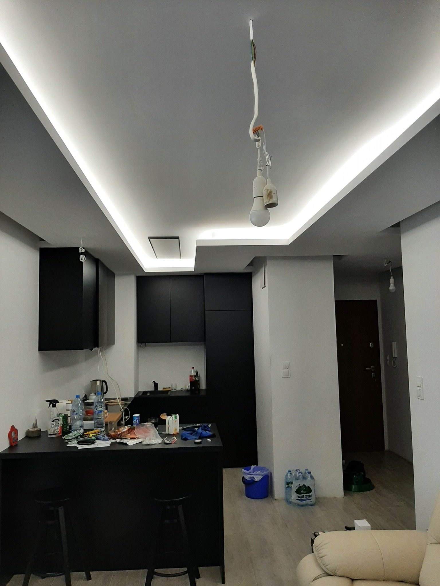 Nowoczesna kuchnia z czarnymi szafkami i listwami LED na suficie, w trakcie montażu oświetlenia - wiszące kable i żarówki tymczasowe.