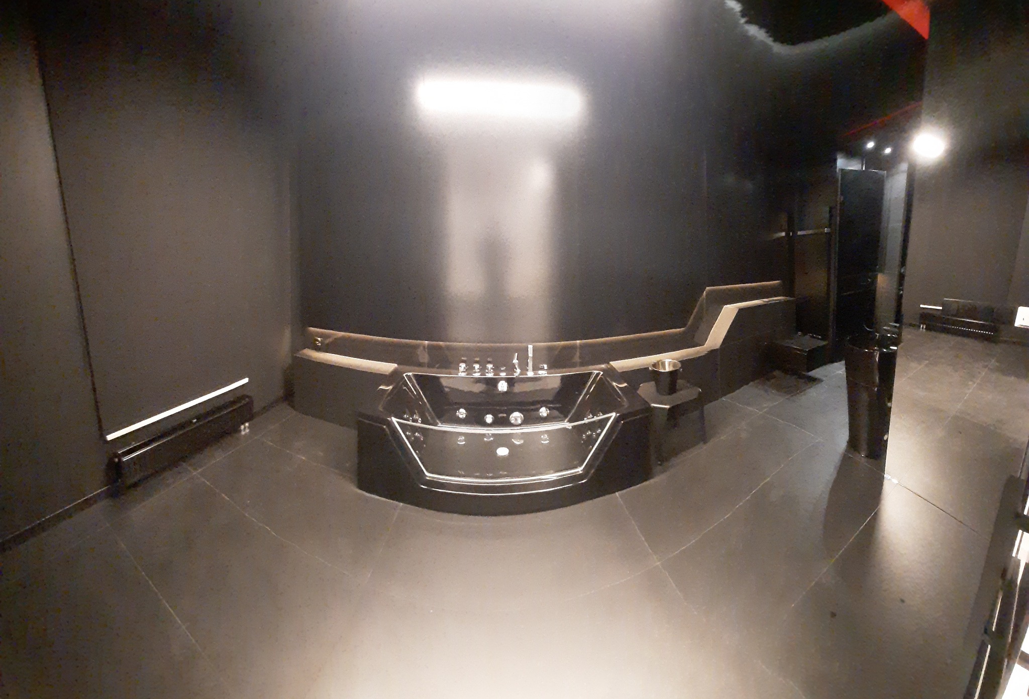 Nowoczesna, czarna wanna z hydromasażem w minimalistycznej łazience z ciemnymi płytkami i oświetleniem punktowym.