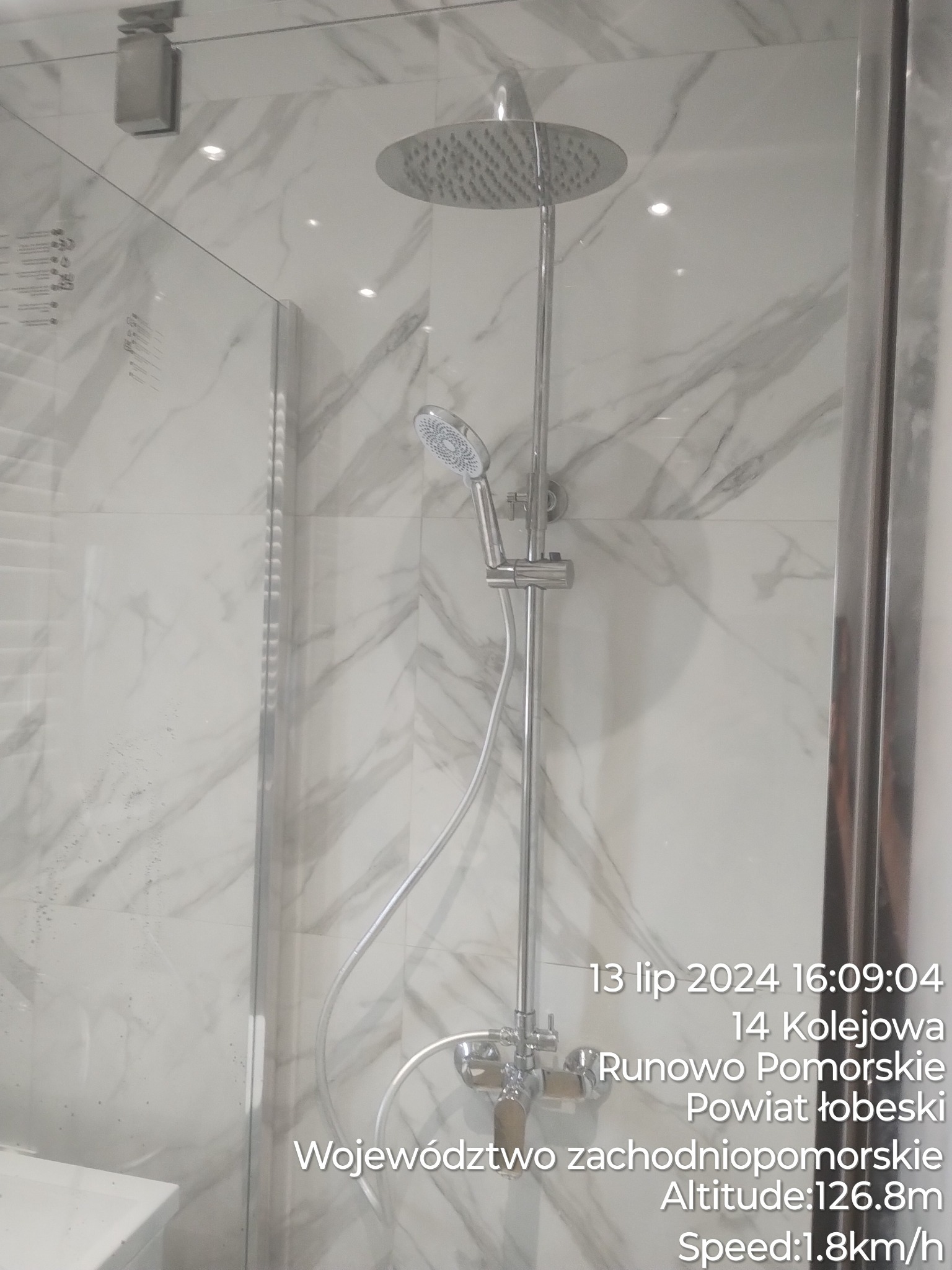 Nowoczesna kabina prysznicowa z deszczownicą i baterią, wykończona płytkami imitującymi marmur.