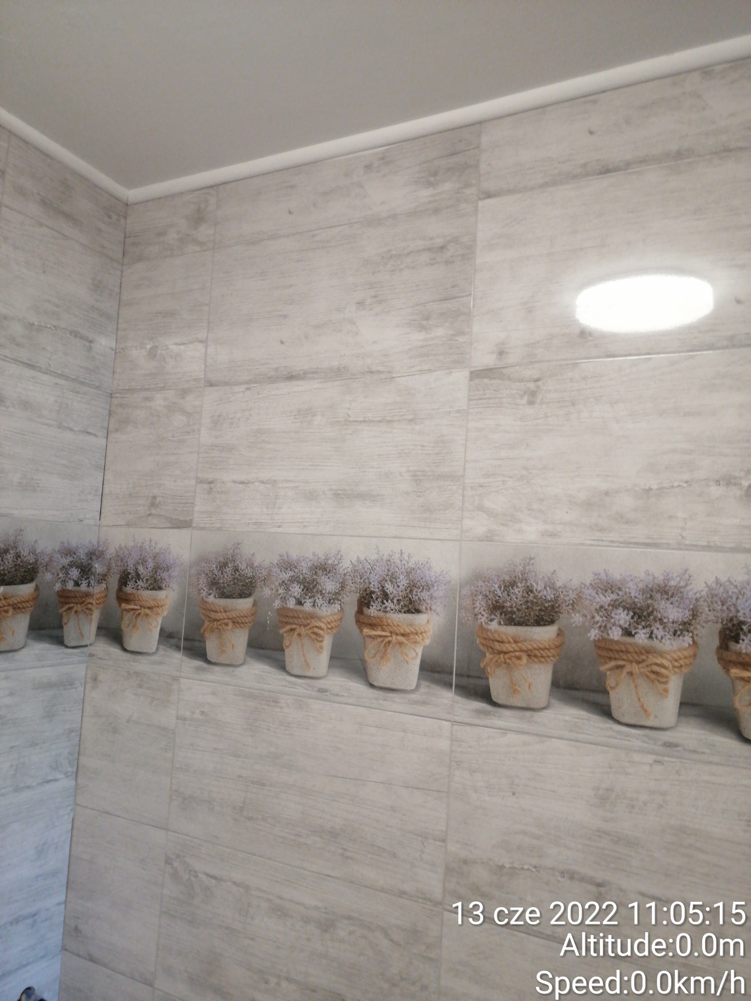 Wykończona łazienka z szarymi płytkami imitującymi drewno i rzędem dekoracyjnych doniczek z lawendą na półce.