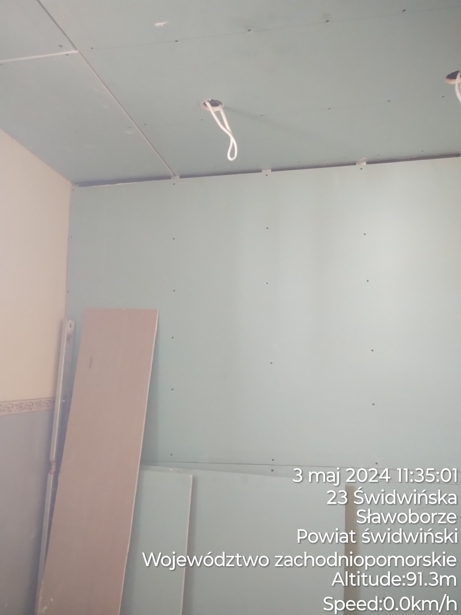 Wnętrze w trakcie remontu: ściany i sufit pokryte płytami gipsowo-kartonowymi, widoczne kable wystające z otworów w suficie, płyta gipsowa oparta o ścianę.