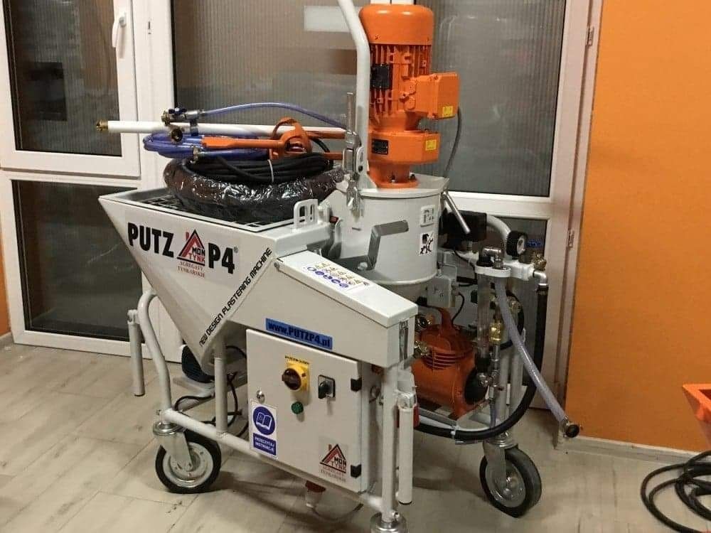 Profesjonalna maszyna do tynkowania Putz P4 na kółkach, z widocznym zbiornikiem, silnikiem i przewodami, ustawiona w jasnym pomieszczeniu z oknem i pomarańczową ścianą.