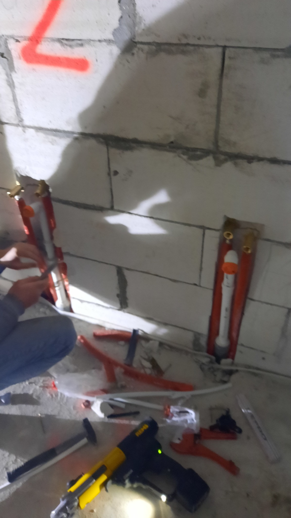 Montaż instalacji grzewczej w surowym wnętrzu: widoczne narzędzia, rury w ścianie z betonu komórkowego i ręce instalatora przy pracy.