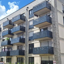 MzGlass - Nowoczesny budynek mieszkalny z balkonami zabezpieczonymi ażurowymi panelami, widok z dołu w słoneczny dzień.