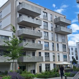 MzGlass - Nowoczesny budynek mieszkalny z balkonami z ażurowymi barierkami, widok z placu zabaw w słoneczny dzień.