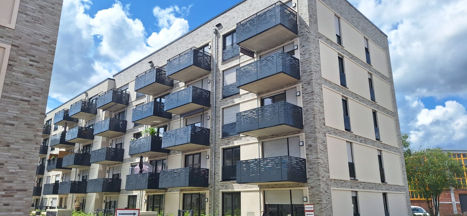 Nowoczesny budynek mieszkalny z balkonami zabezpieczonymi ażurowymi panelami, widok z dołu w słoneczny dzień.