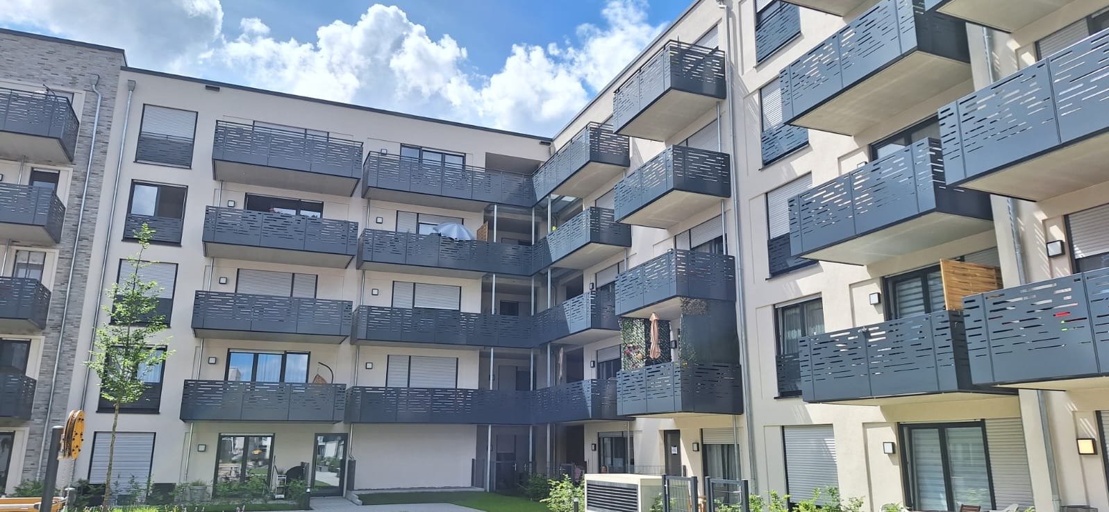 Nowoczesny budynek wielorodzinny z balkonami zabezpieczonymi metalowymi balustradami o ażurowym wzorze, widok z dołu w słoneczny dzień.