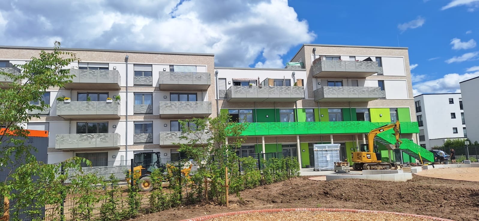 Nowoczesny budynek wielorodzinny w Świdwinie z balkonami z szarymi ażurowymi balustradami, widok na plac budowy z żółtą koparką i przygotowanym terenem.