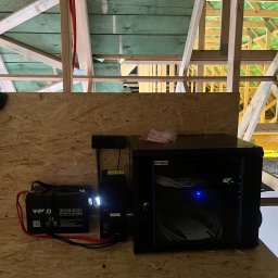 ENERGONOBIS SPÓŁKA Z OGRANICZONĄ ODPOWIEDZIALNOŚCIĄ - Zestaw akumulatorowy V-Pro i szafa rack z okablowaniem w surowym wnętrzu poddasza z widoczną konstrukcją dachu. Elementy systemu zasilania awaryjnego.