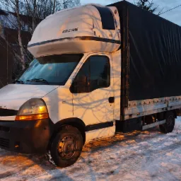 Biały samochód dostawczy Renault Master z czarną plandeką na skrzyni ładunkowej, zaparkowany na śniegu, z napisem 'MOBILE HOME' na kabinie.