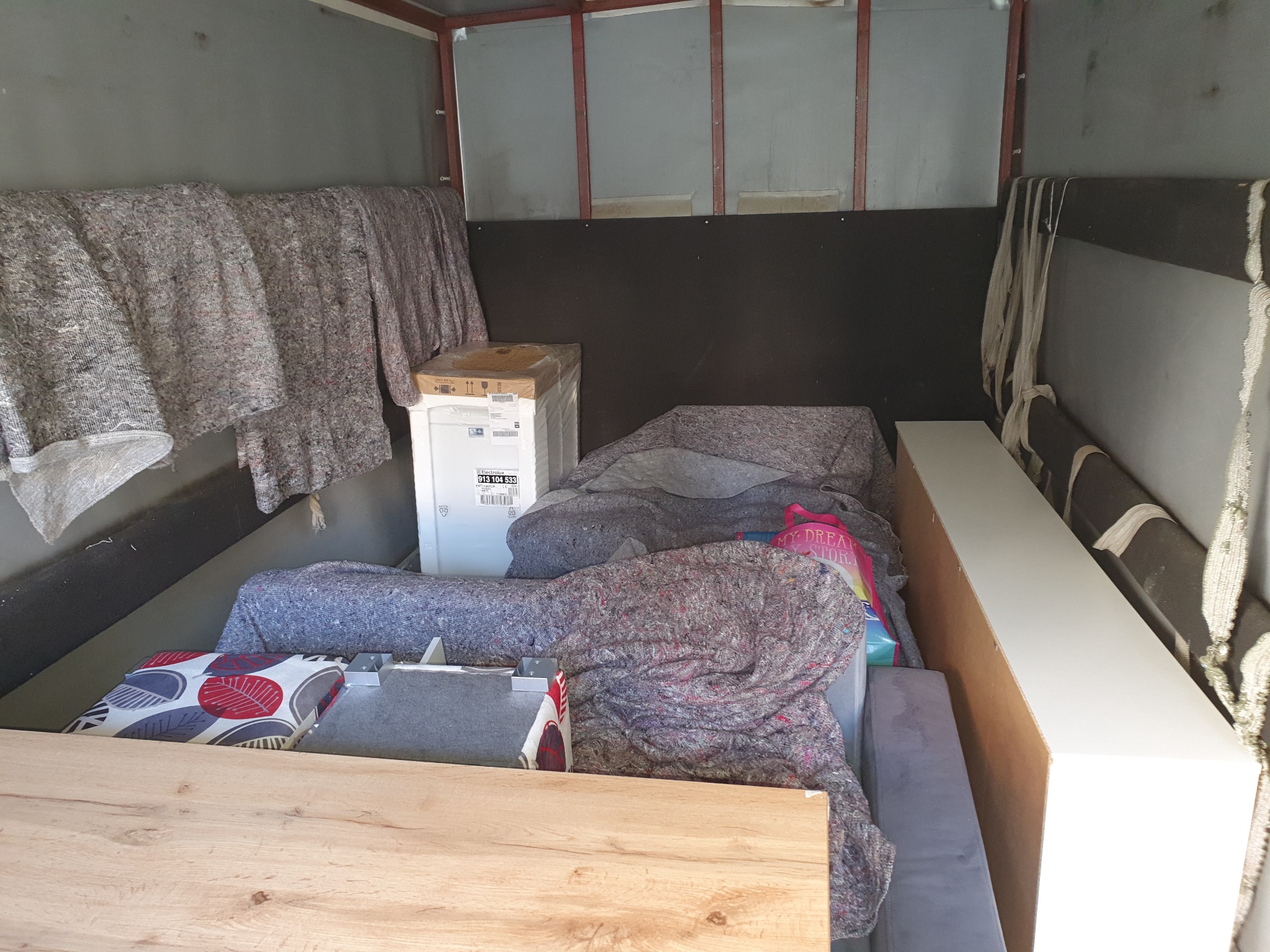 Wnętrze przestrzeni ładunkowej pojazdu transportowego, zabezpieczone koce i kartony z zapakowanymi przedmiotami gotowymi do przewozu.