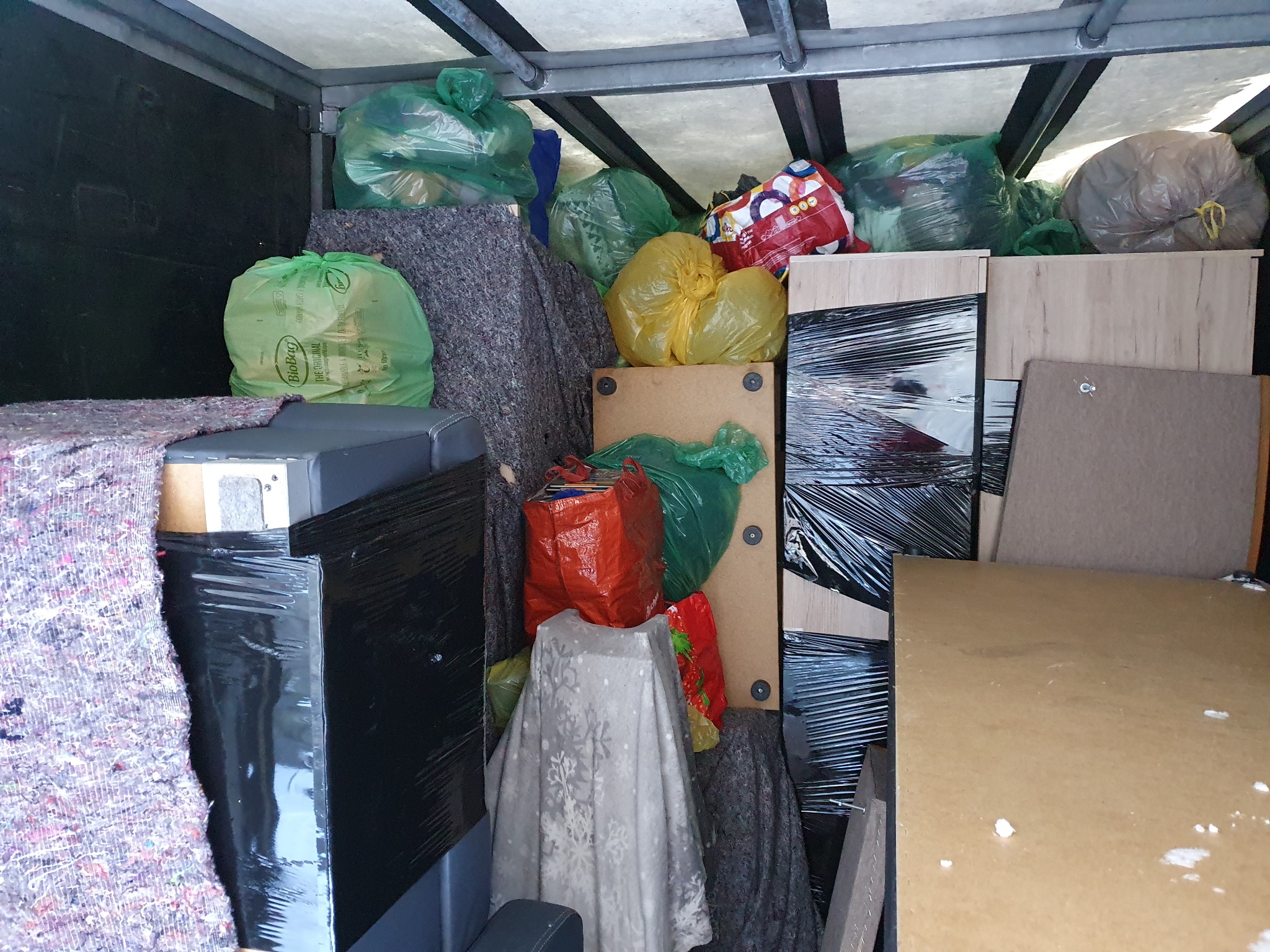 Wnętrze samochodu dostawczego wypełnione różnymi przedmiotami zabezpieczonymi folią stretch, workami na śmieci i kocami transportowymi.