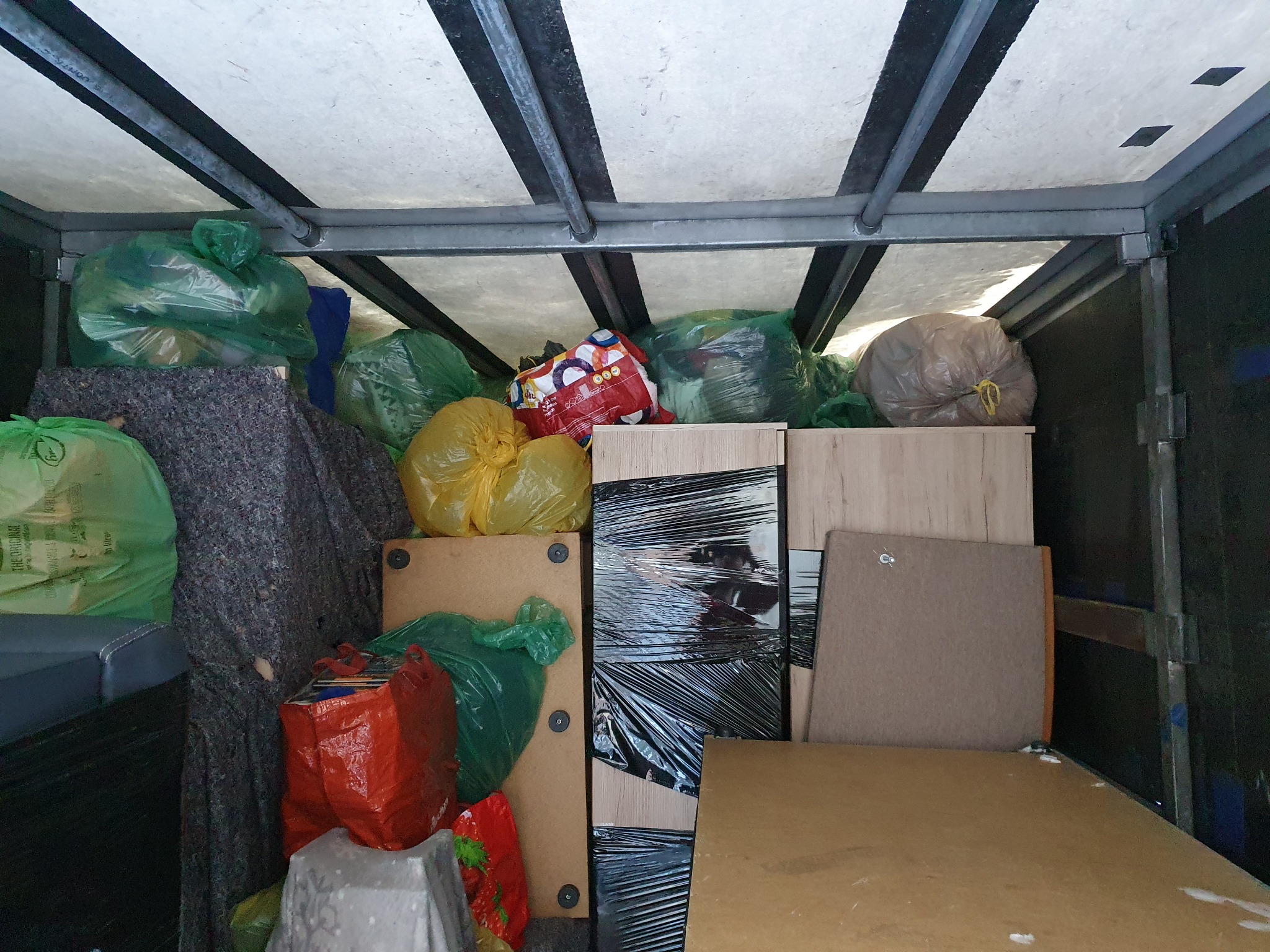 Wnętrze paki transportowej wypełnione workami z rzeczami i meblami zabezpieczonymi folią stretch podczas przeprowadzki.