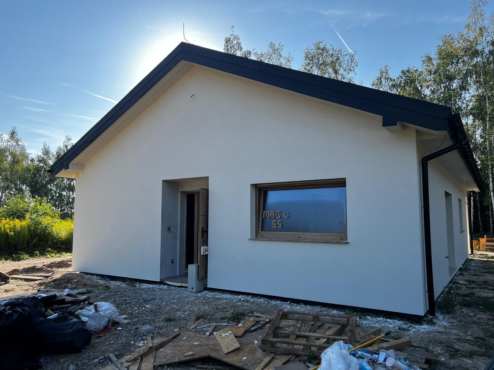 Surowy stan elewacji parterowego domu jednorodzinnego w Gołkowicach Dolnych z ciemną stolarką okienną i czarnym dachem, widoczne ślady budowy i resztki materiałów budowlanych.