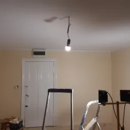 Pokój po odświeżeniu koloru ścian na beżowo, widoczna drabina, lampa wisząca na kablu, dwie pary drzwi z białymi framugami.