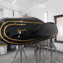 Czarny, błyszczący element karoserii motocykla z żółtymi zdobieniami i napisem 'Jurek' na metalowym stojaku w warsztacie blacharsko-lakierniczym.