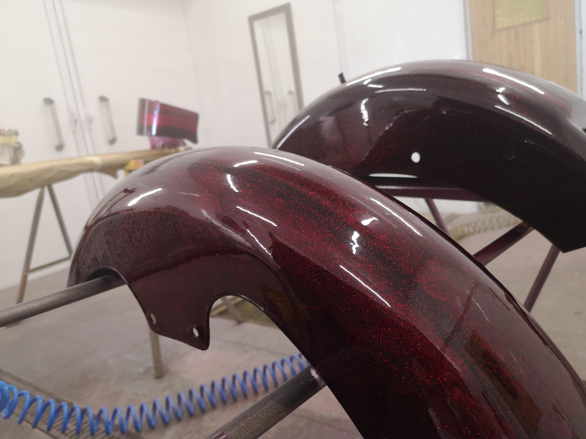 Dwa błotniki motocyklowe w kolorze ciemnej wiśni z brokatowym wzorem, suszone w lakierni.