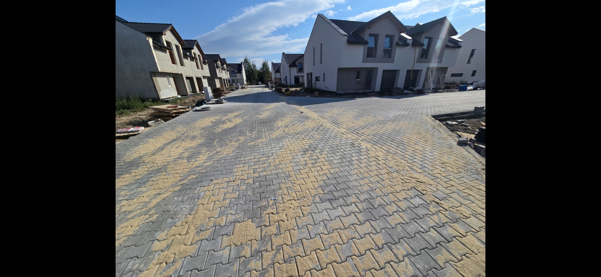 Nowo ułożona szara kostka brukowa z piaskiem wypełniającym szczeliny na osiedlu domów jednorodzinnych w trakcie budowy, widok z perspektywy ulicy.