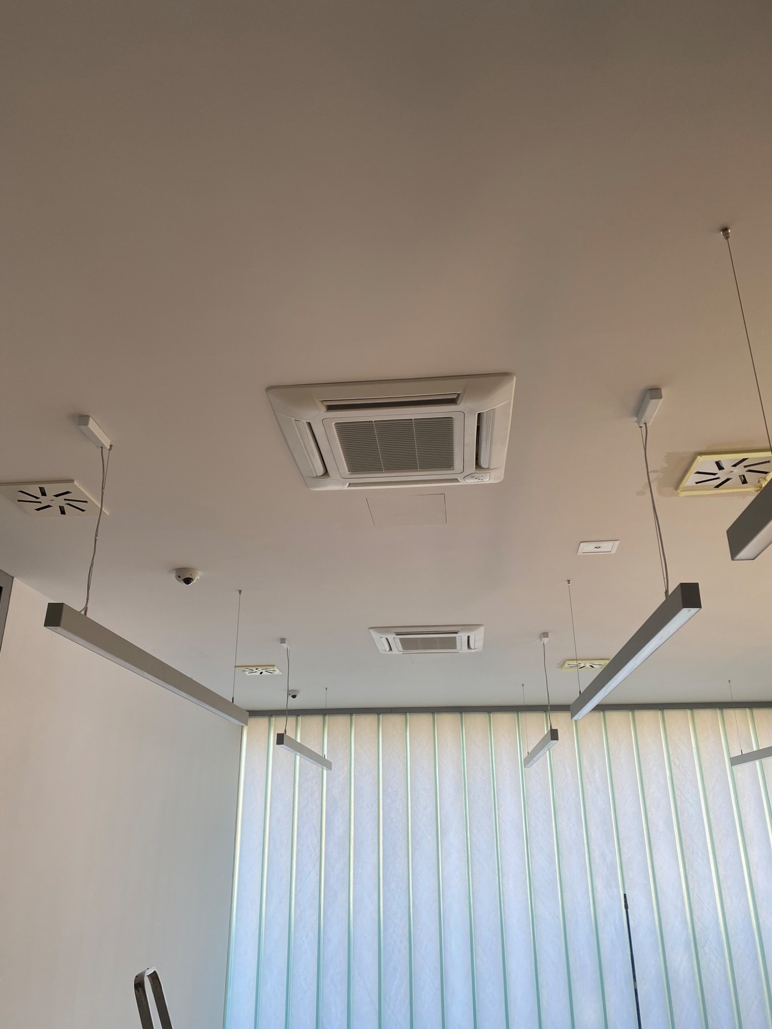Sufit biurowy z zamontowanymi kasetonowymi klimatyzatorami, liniowymi lampami LED i kamerą monitoringu.