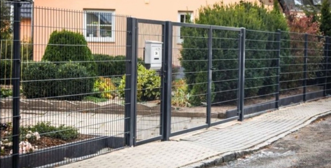 Nowoczesne ogrodzenie panelowe z bramą otwieraną na posesję z kostki brukowej, na słupku furtki skrzynka pocztowa.