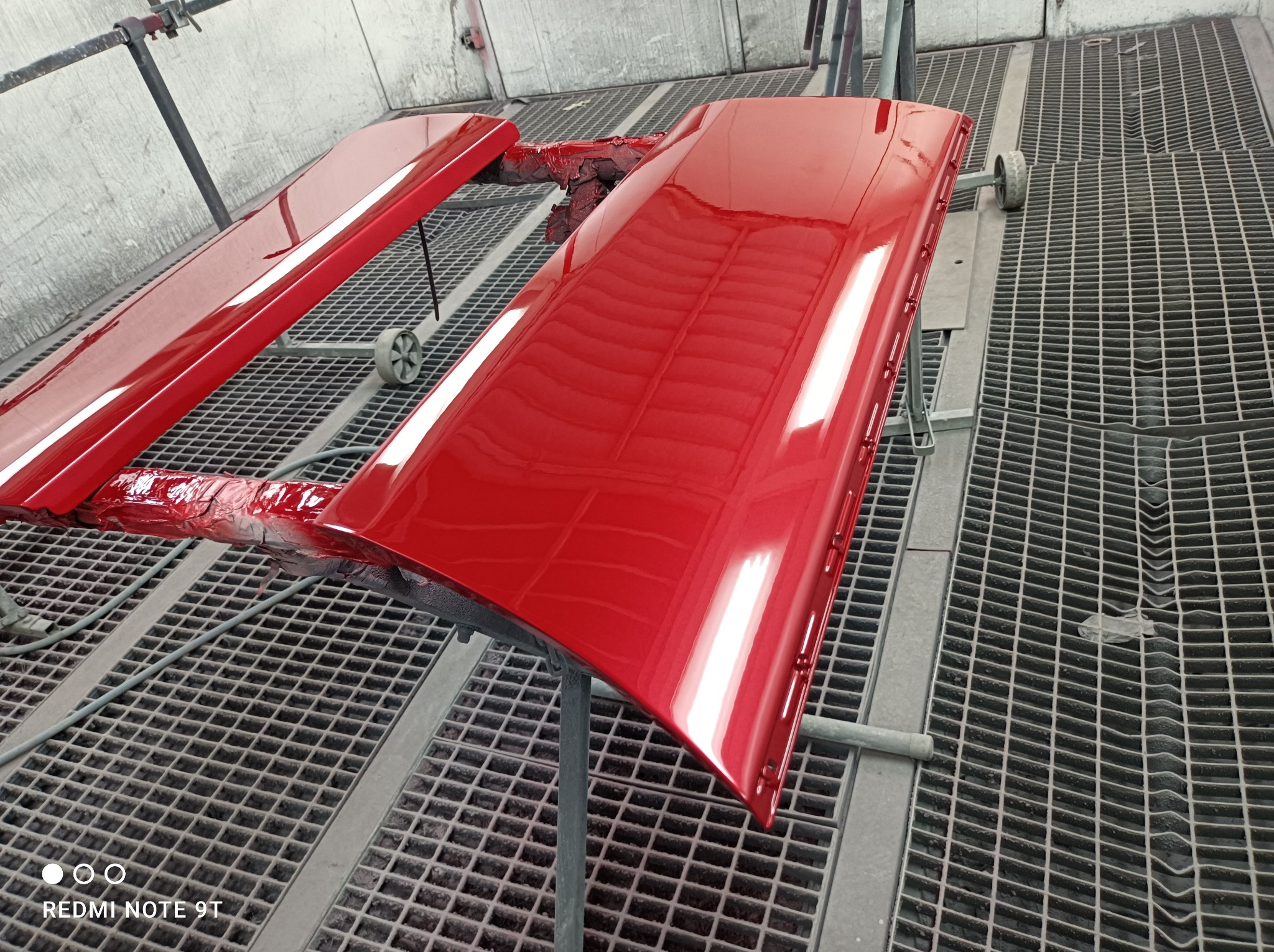 Czerwone, błyszczące elementy karoserii samochodowej po lakierowaniu, suszone w lakierni na metalowej kratownicy.