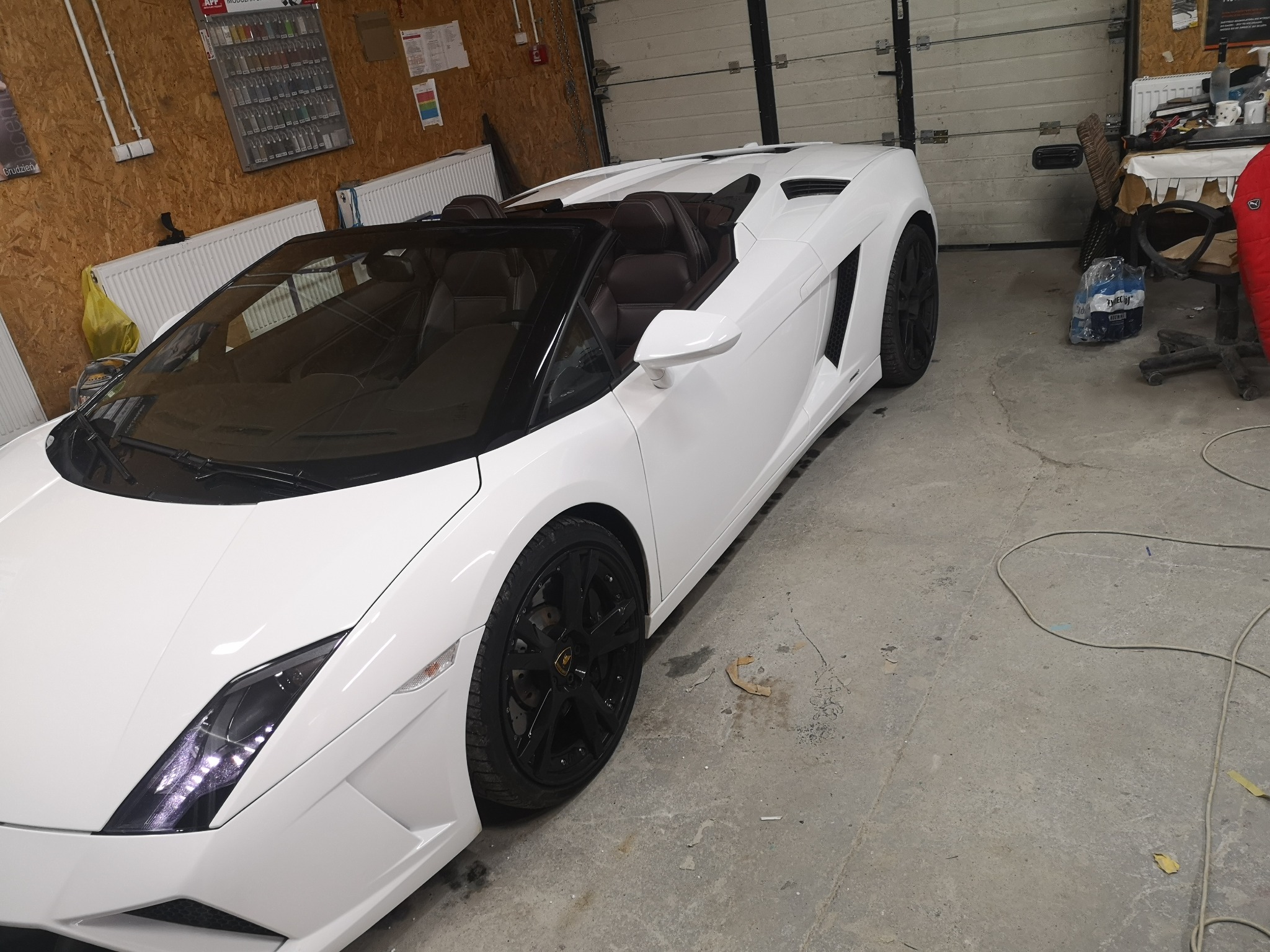 Białe Lamborghini Gallardo Spyder z czarnymi felgami, po renowacji lakieru, stoi w warsztacie.