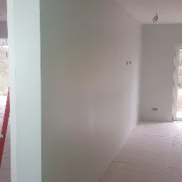 Świeżo pomalowane na biało wnętrze w trakcie remontu, podłoga zabezpieczona folią, widoczne kable i puszka farby, fragment drabiny oparty o ścianę.