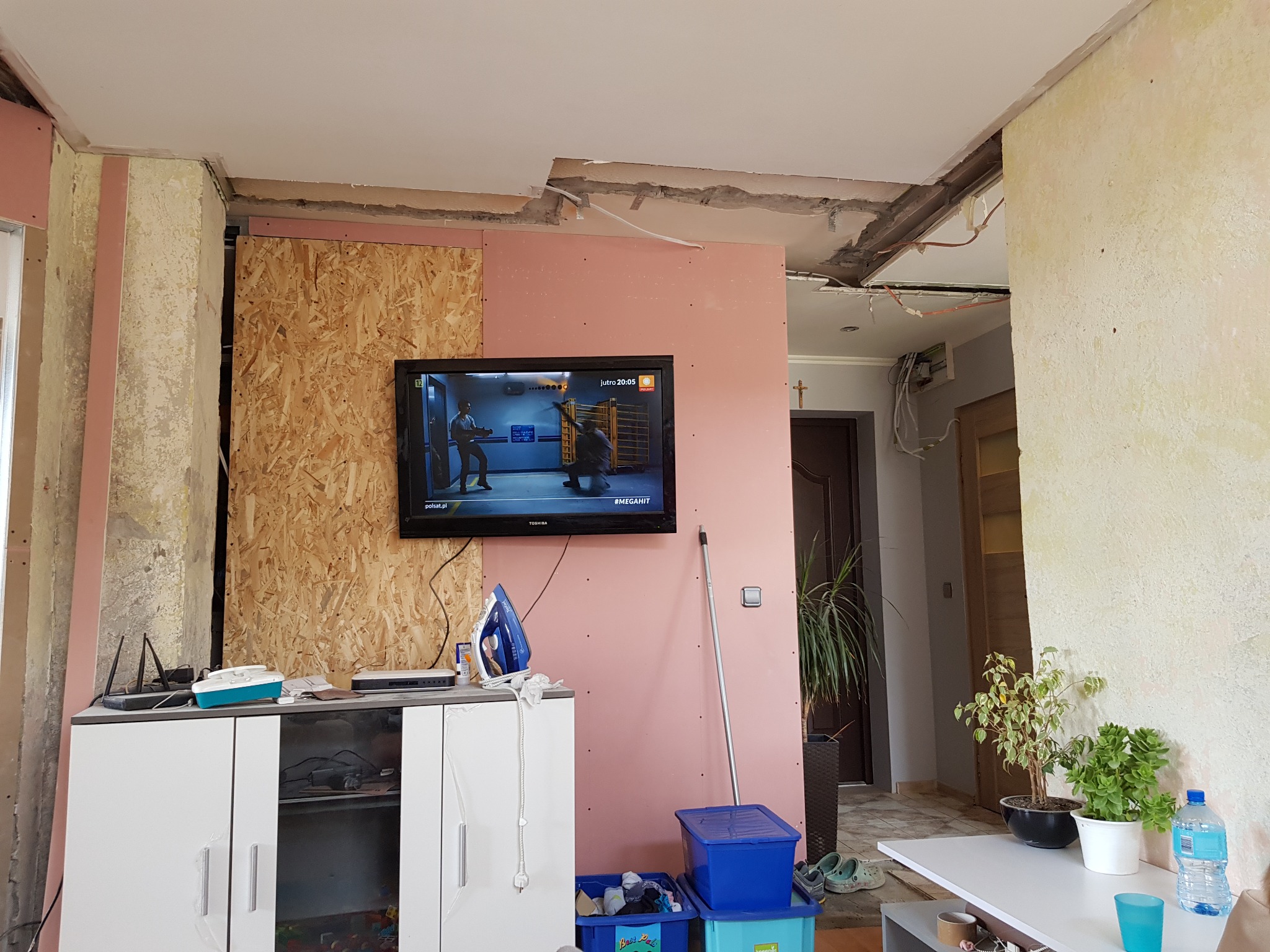 Wnętrze pokoju w trakcie prac wykończeniowych: ściana z płyt gipsowo-kartonowych pomalowana na różowo, odsłonięty sufit z widocznymi kablami, fragment ściany z płyt OSB, meble z żelazkiem...